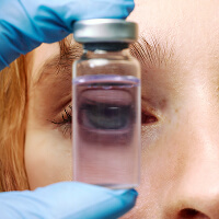 A gloved hand holding a vial up in front of a patient’s face