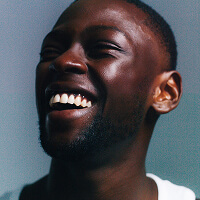 A man laughing, head tilted back, against a plain wall