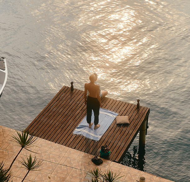 A person standing on a wooden jetty above still water at sunrise