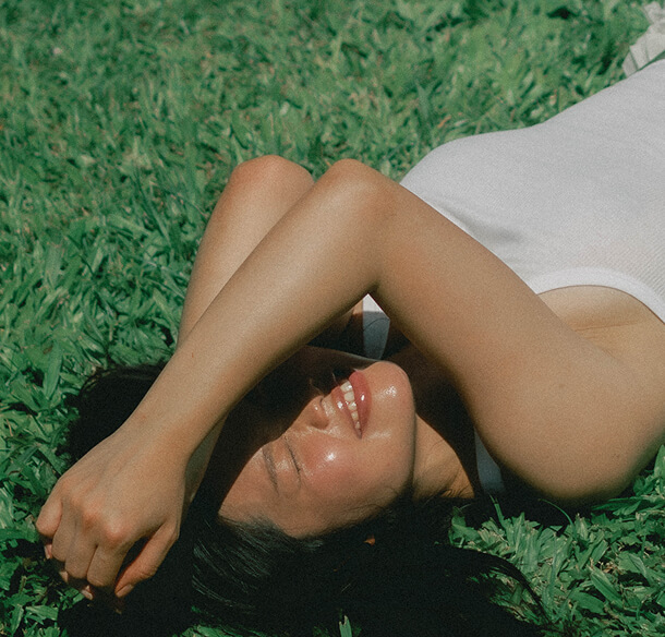 A woman lying on grass in bright sun, an arm across her face