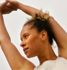 A woman standing in soft daylight, arms raised above her head
