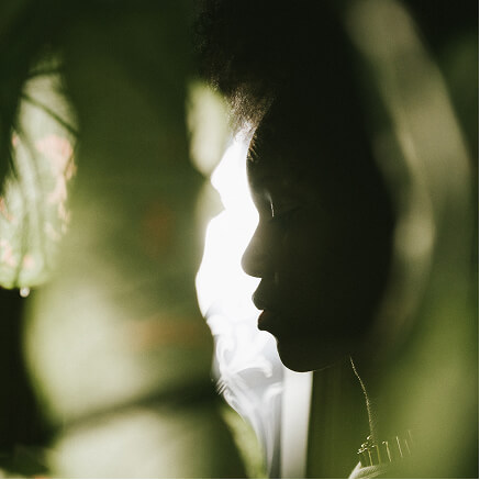 A figure in profile against dark green foliage, lit from behind