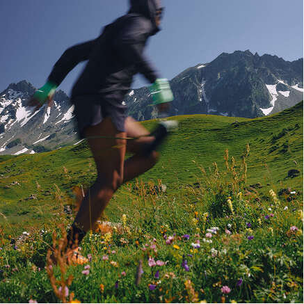 A runner crossing a wildflower meadow below a snow-streaked ridge