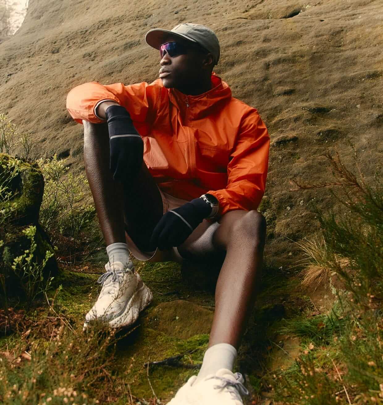 A man in an orange jacket sitting on a mossy hillside
