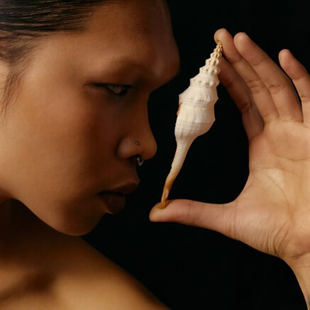 A woman in profile holding a spiral shell to her ear