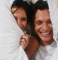 Two people laughing together under a white duvet
