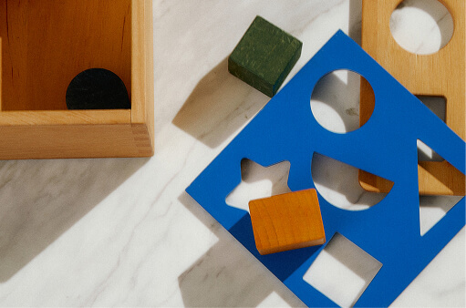 Wooden blocks beside a blue shape-sorter board in low sunlight
