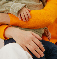 A child’s hands resting in an adult’s, sleeves in orange and cream