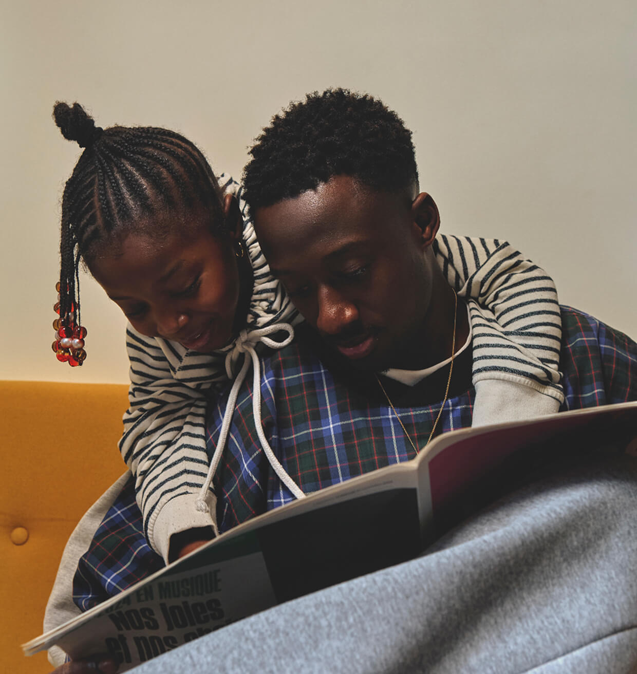 A father and daughter reading a magazine together on a yellow sofa