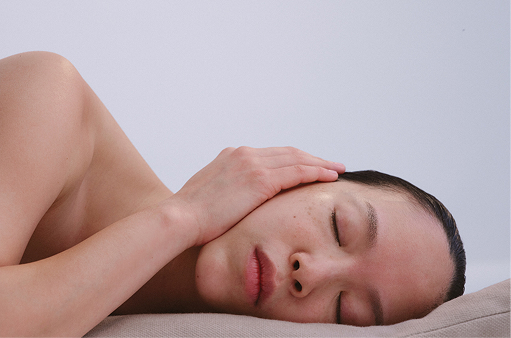 A person lying down with their eyes closed, a hand resting against their cheek