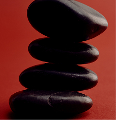 Smooth dark stones stacked in front of a deep red backdrop
