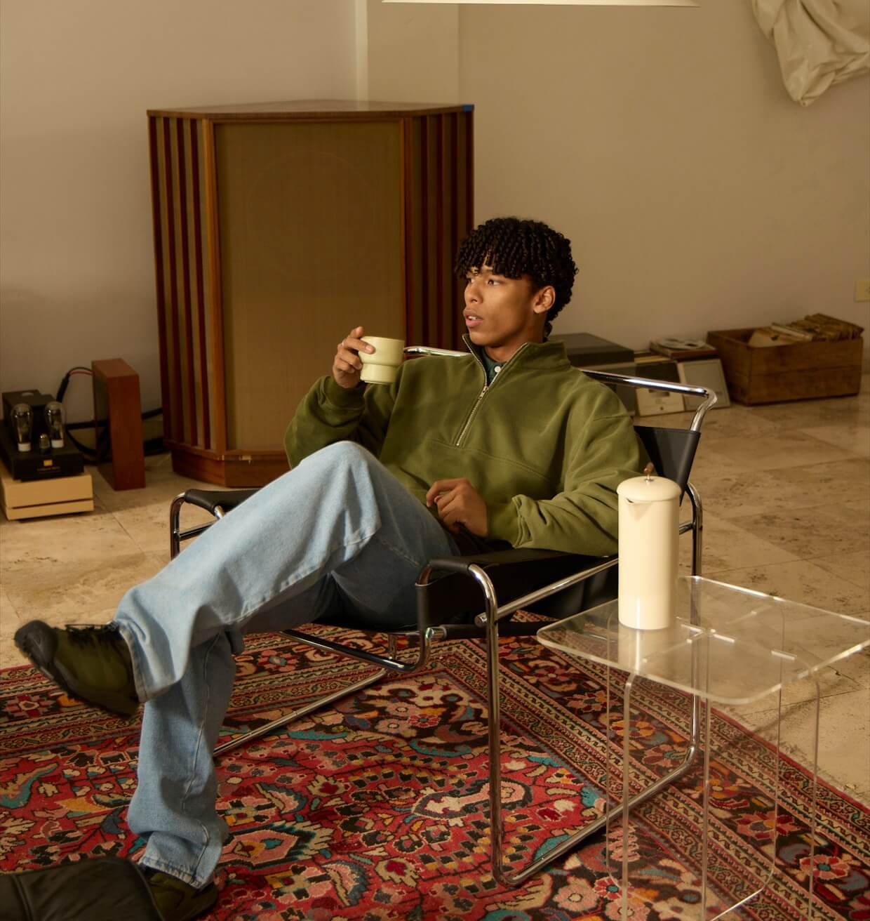 A man sitting back in a low chair with a mug, morning light across the room