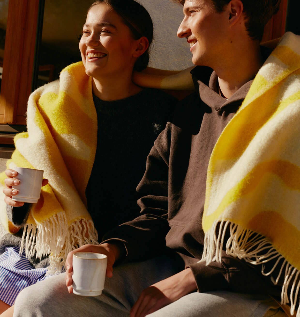 Two patients sitting together under a blanket, holding warm drinks